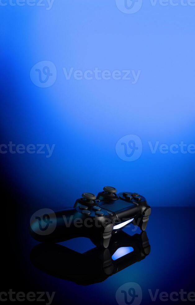 Black gamepad with backlight on blue back. Joystick on glossy surface. photo
