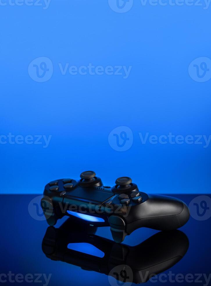 Black gamepad with backlight on blue back. Joystick on glossy surface. photo