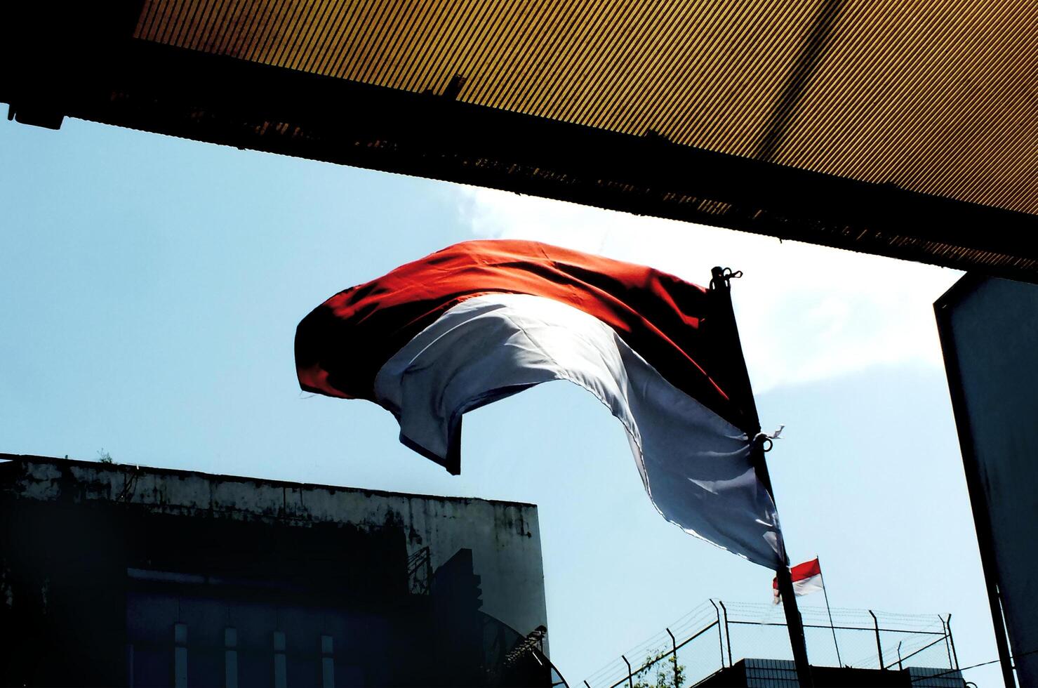 Indonesia national flag waving in the wind between city building and public facility with clear blue sky background. Nation patriotism. The Hari Kemerdekaan Indonesia photo