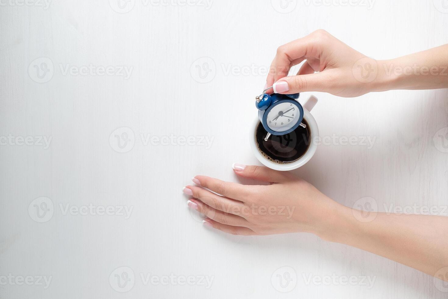 hands of a young girl holding a cup of coffee and alarm clock photo