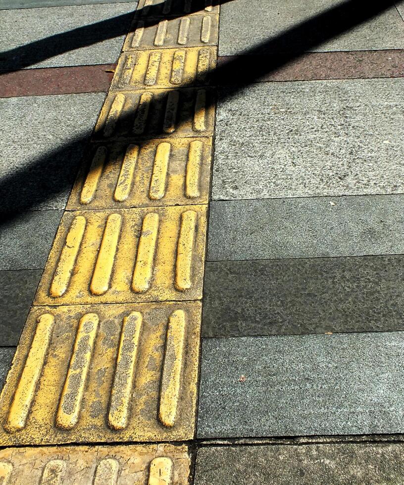 abstract background textured of a long shadow on an embossed yellow line pavement for blind pedestrian. photo