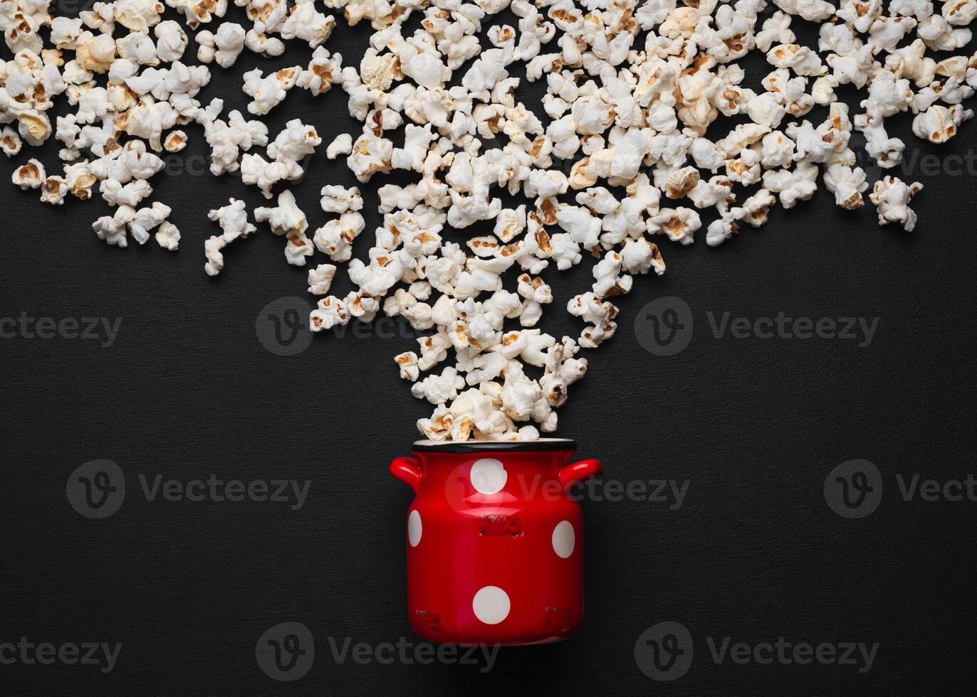 popcorn on a dark background, pouring out of a red can with white polka dots photo