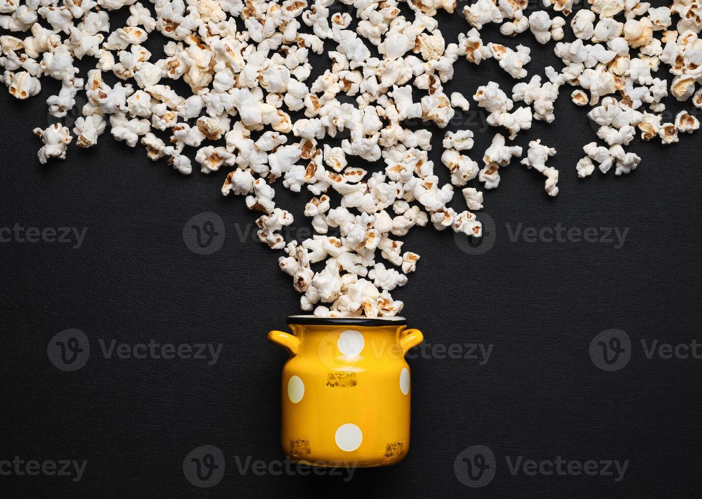 popcorn on a dark background, pouring out of a yellow can with white polka dots photo