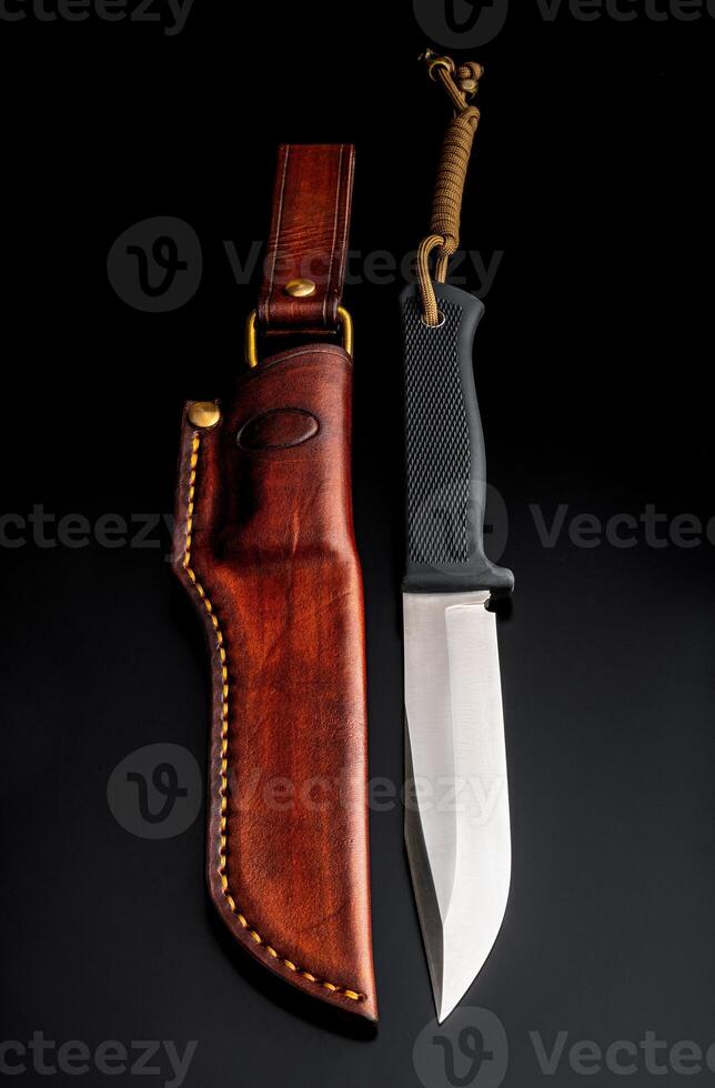 A modern hunting knife and a leather case for him on a dark background. Melee weapons for hunting and self-defense. The instrument of crime. photo