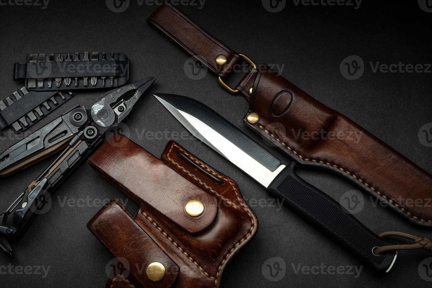 Hunting knife and multitool on a dark background. Brown leather cases near the knife and multitool. Postcard concept for men. photo