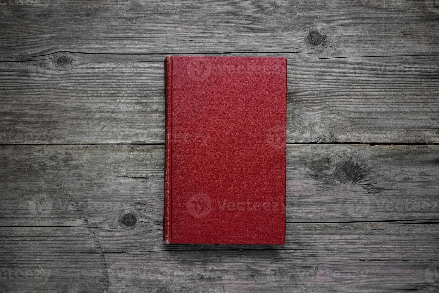A closed book on an old wooden table. Red hard cover. Vintage back. photo