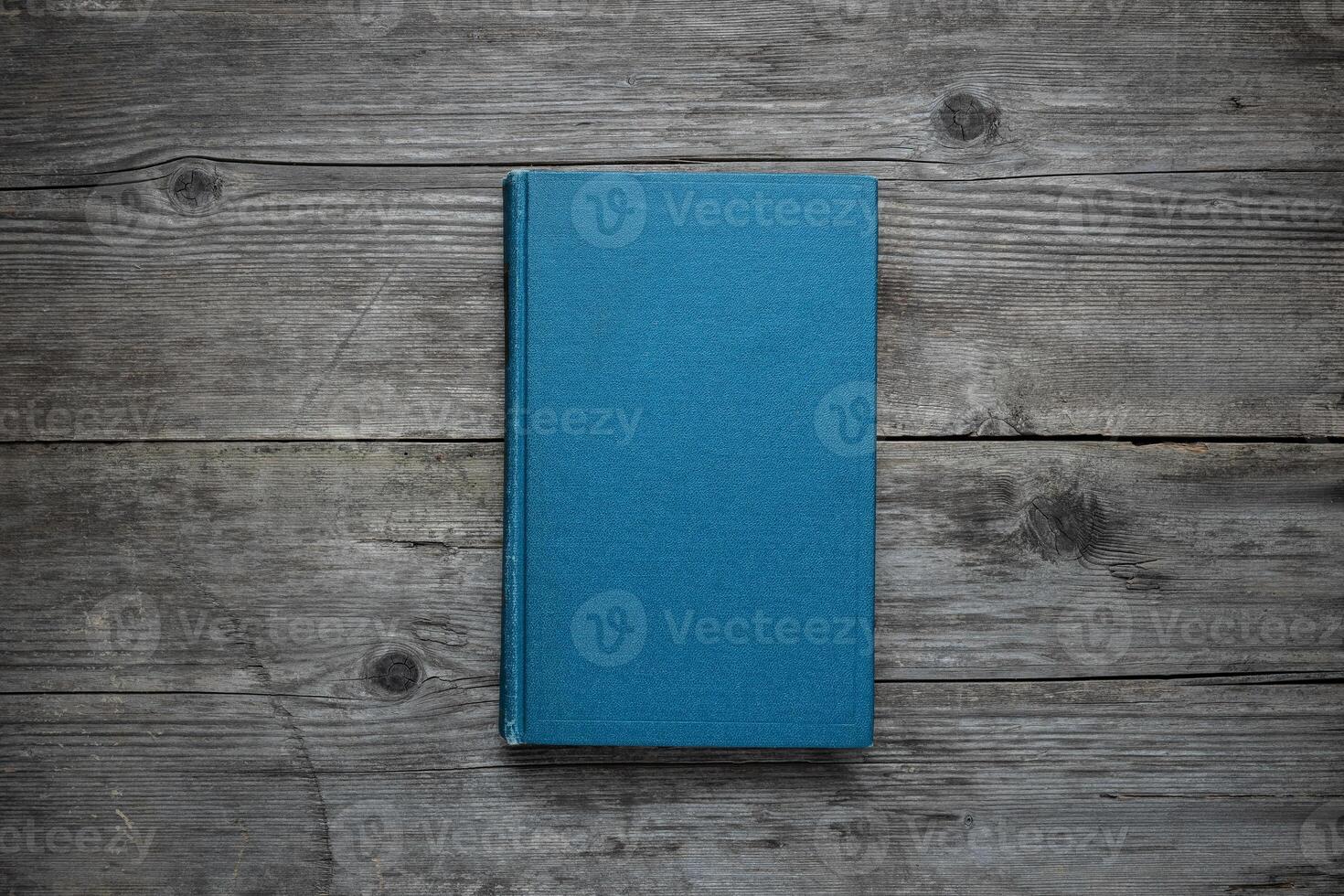 A closed book on an old wooden table. Blue hard cover. Vintage back. photo