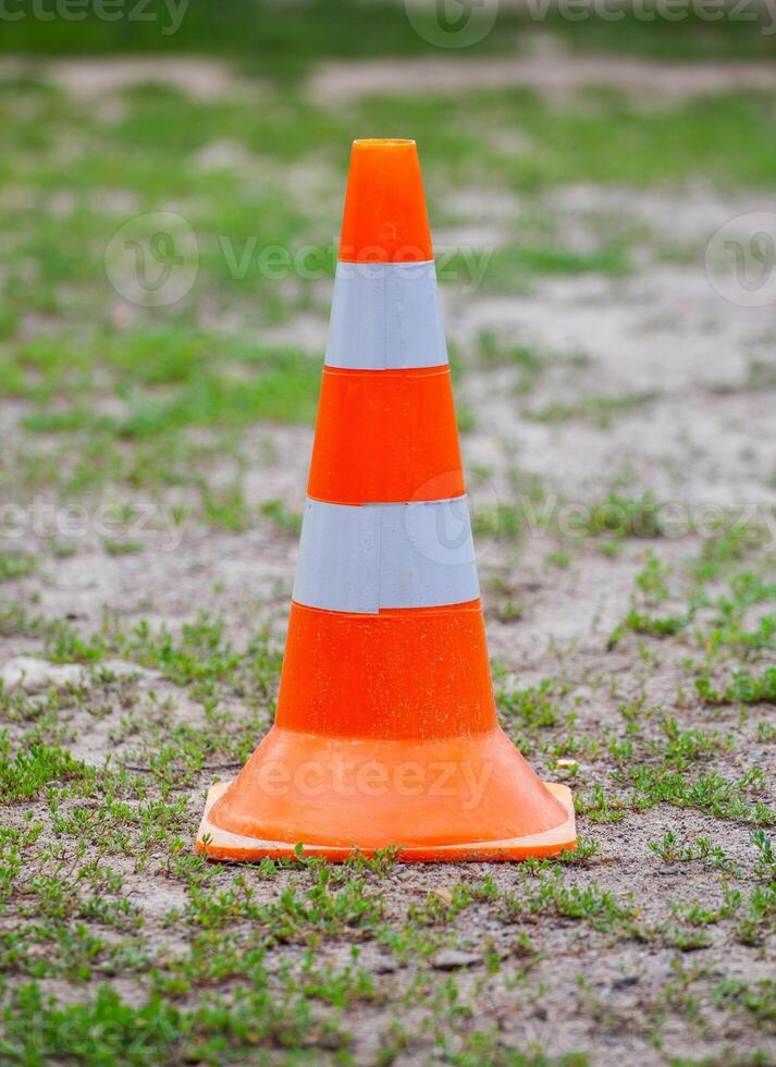 Orange road cone with white stripes on a back of green grass. photo