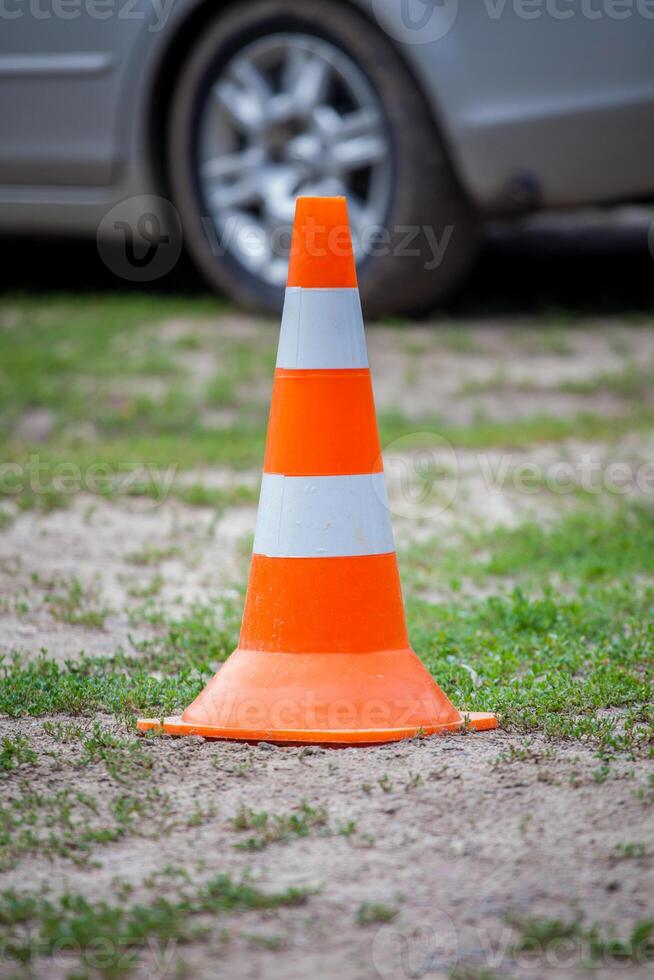 Orange road cone with white stripes on a background of green grass. A car in the back. photo