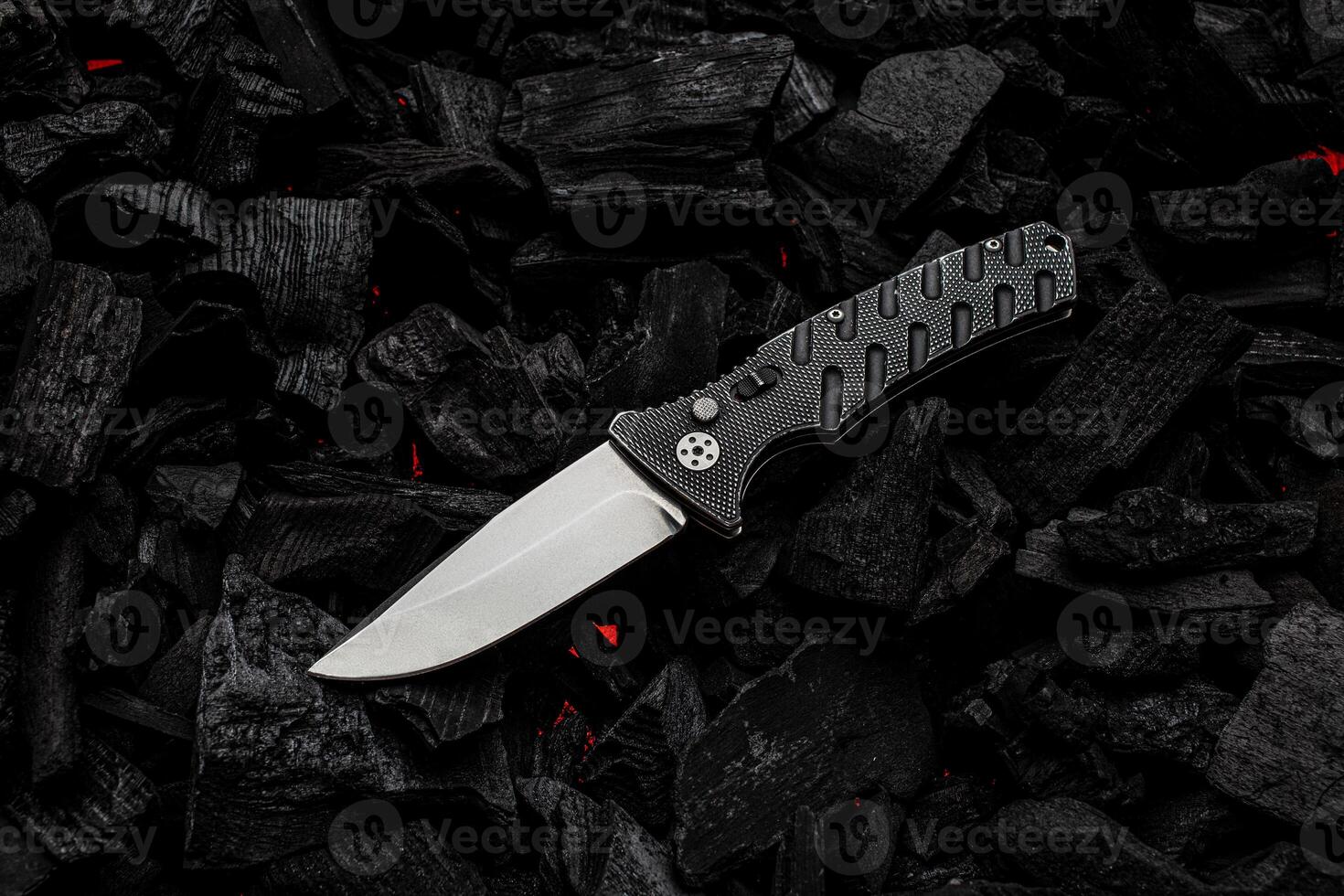 Folding knife on charcoal with red streaks of heat. Dark back. photo