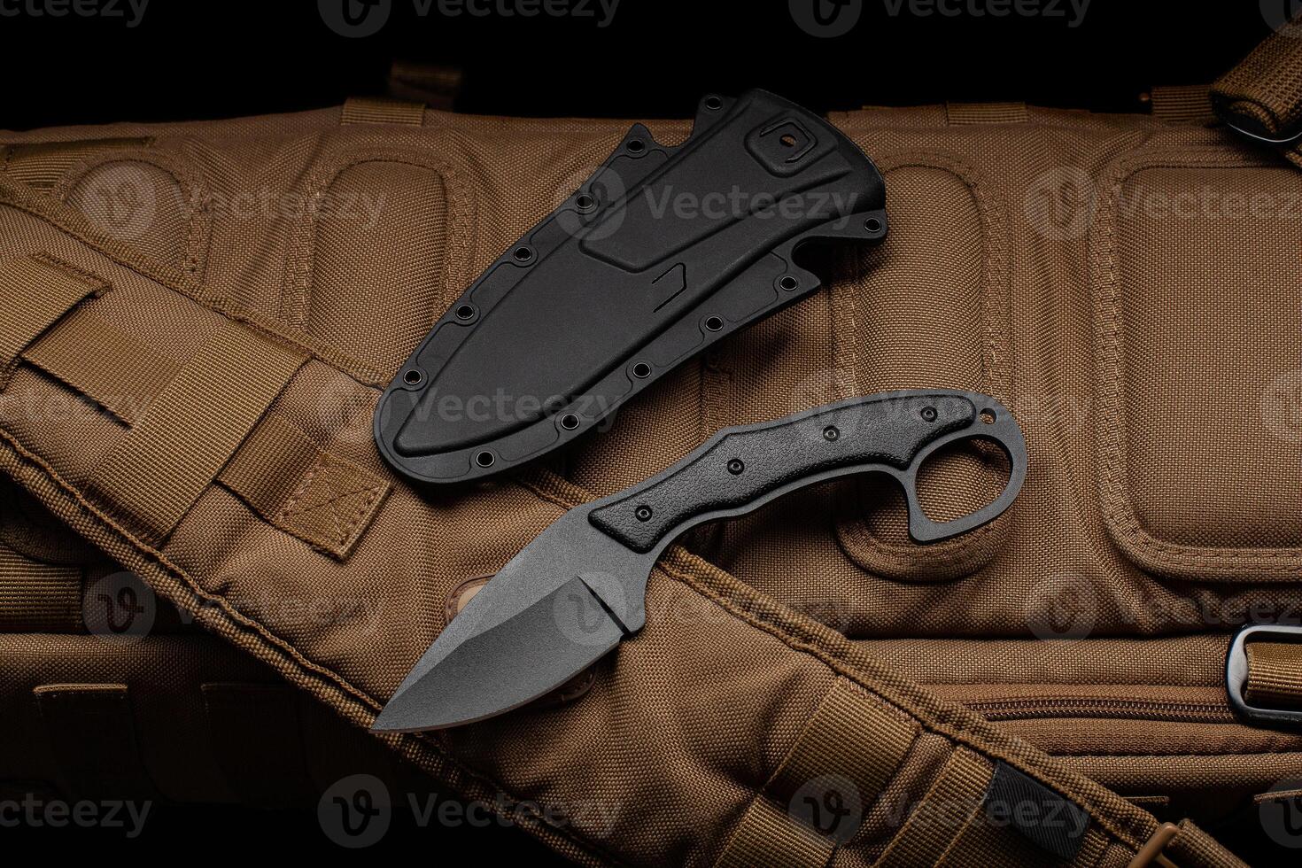 A small knife with a plastic sheath on a sand-colored military backpack. Dark back. photo