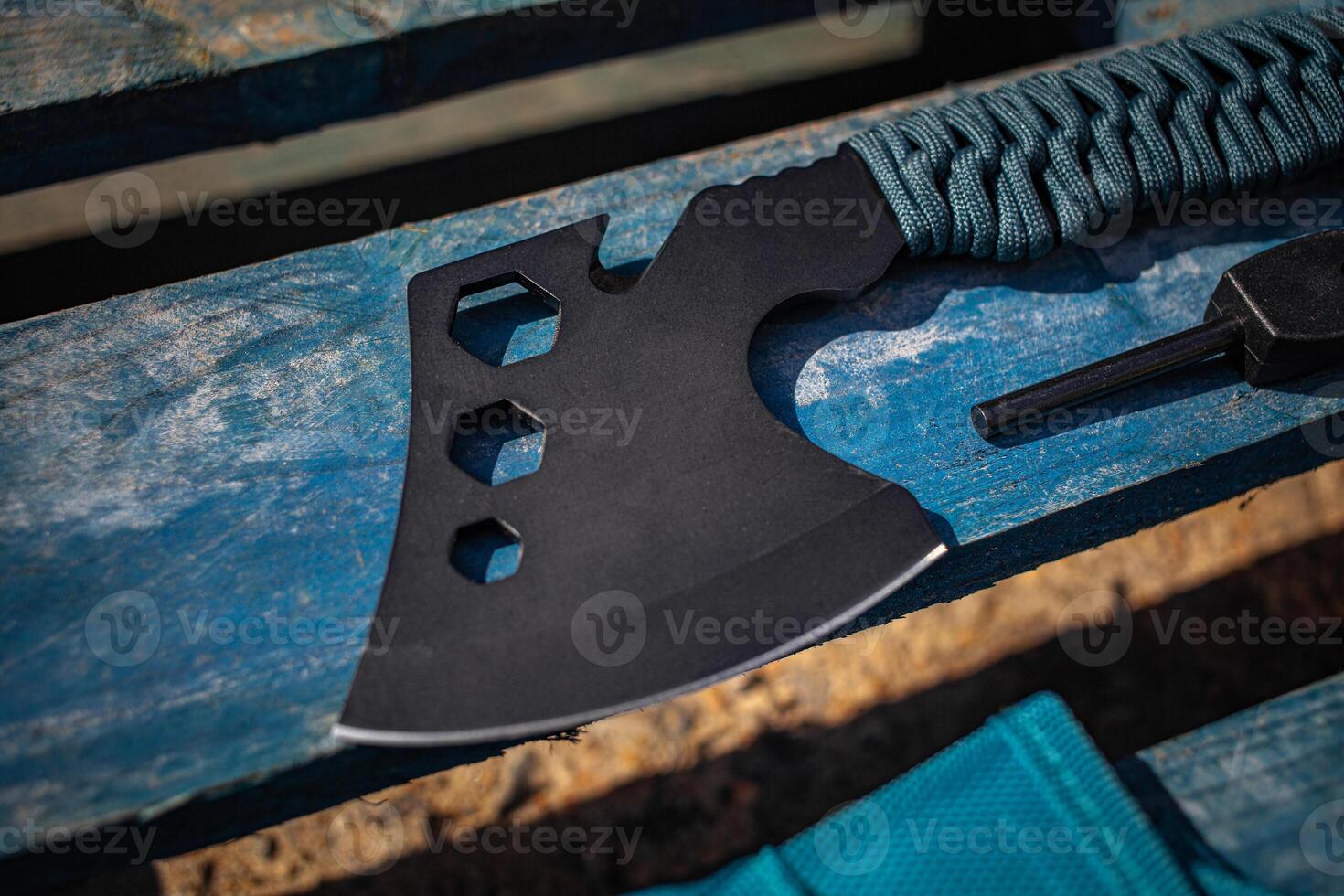 A small black ax with a paracord-wrapped handle. A tool for cutting branches or firewood in the forest. Self defense weapon. Wooden back. photo
