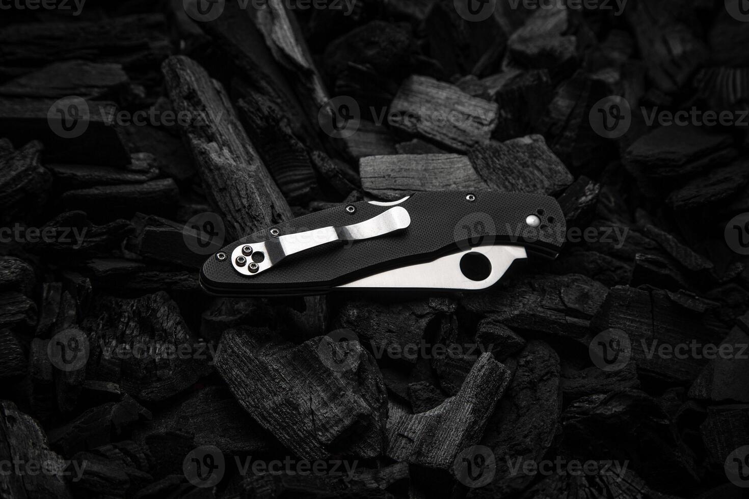 Modern knife with a silver blade. Hunting, military folding knife on smoldering charcoal. Black back. photo