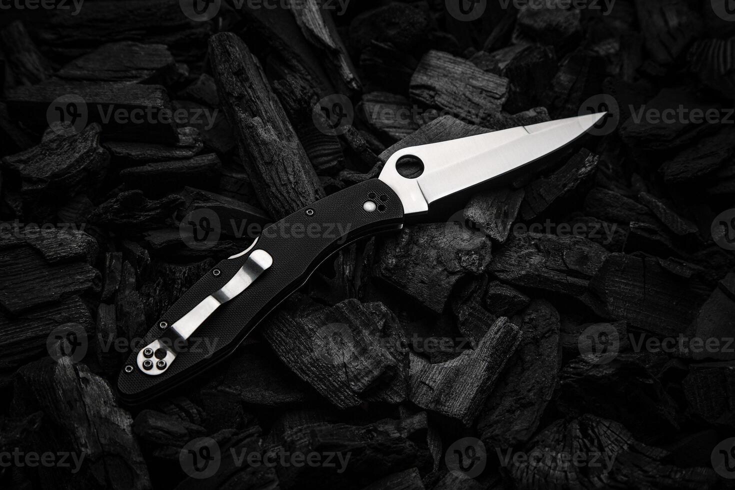 Modern knife with a silver blade. Hunting, military folding knife on smoldering charcoal. Black back. photo