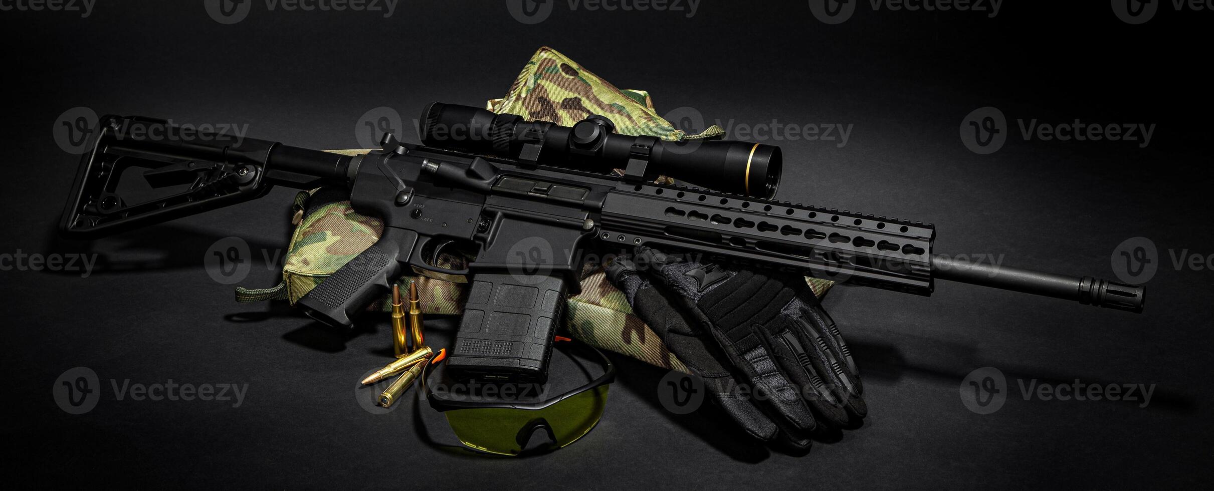 Modern automatic carbine with optical sight. Tactical goggles cartridges and gloves near weapons. Dark back. photo