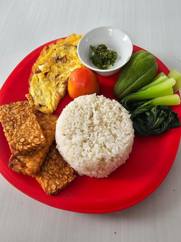A simple lunch plate consisting of rice, omelet and some vegetables plus green chili sauce photo