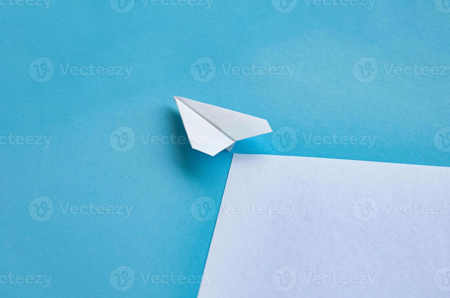 Angle view of paper airplane flying on blue background with customizable space for text photo
