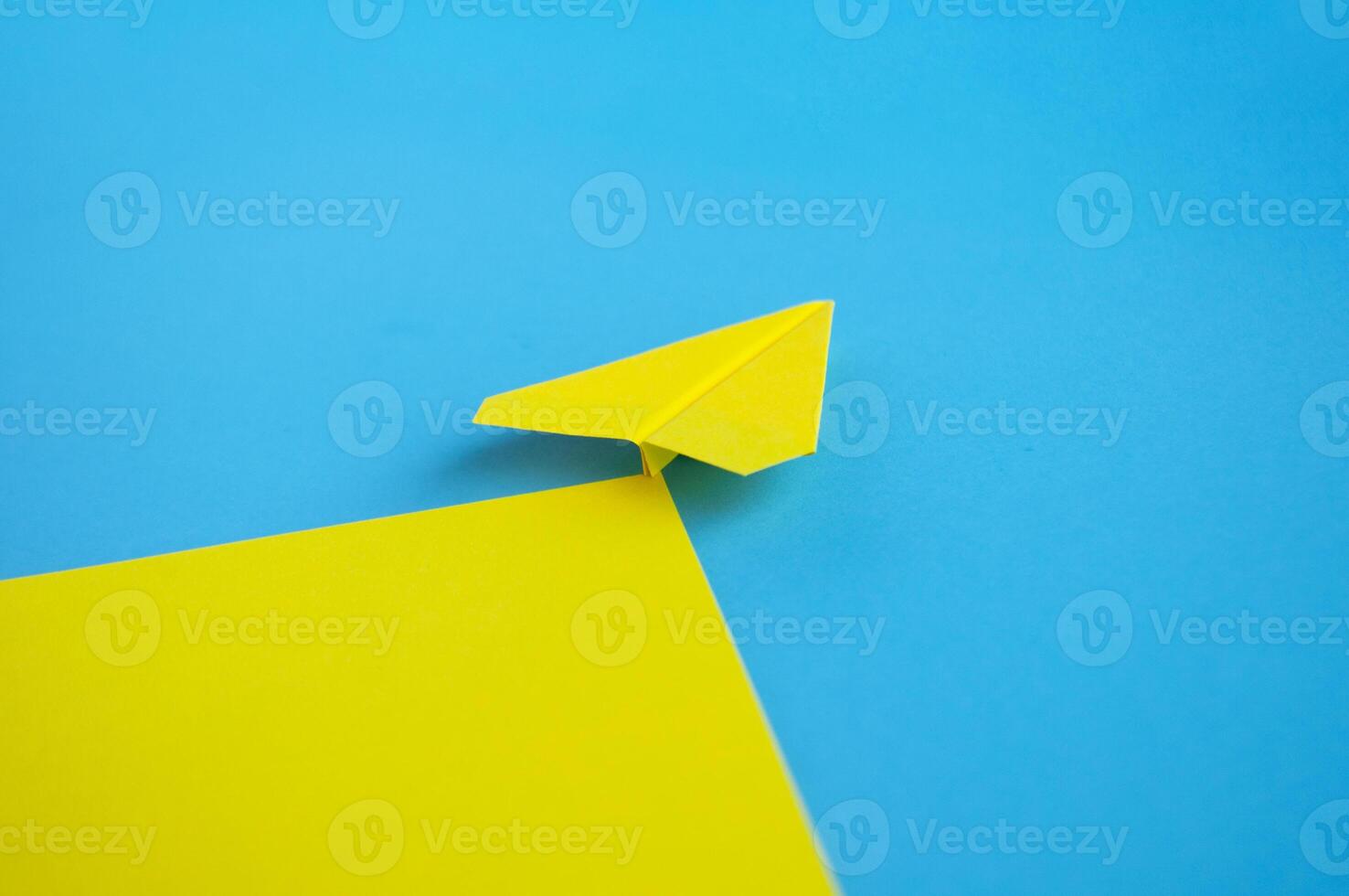 View from behind of yellow paper airplane flying along the route on blue background photo