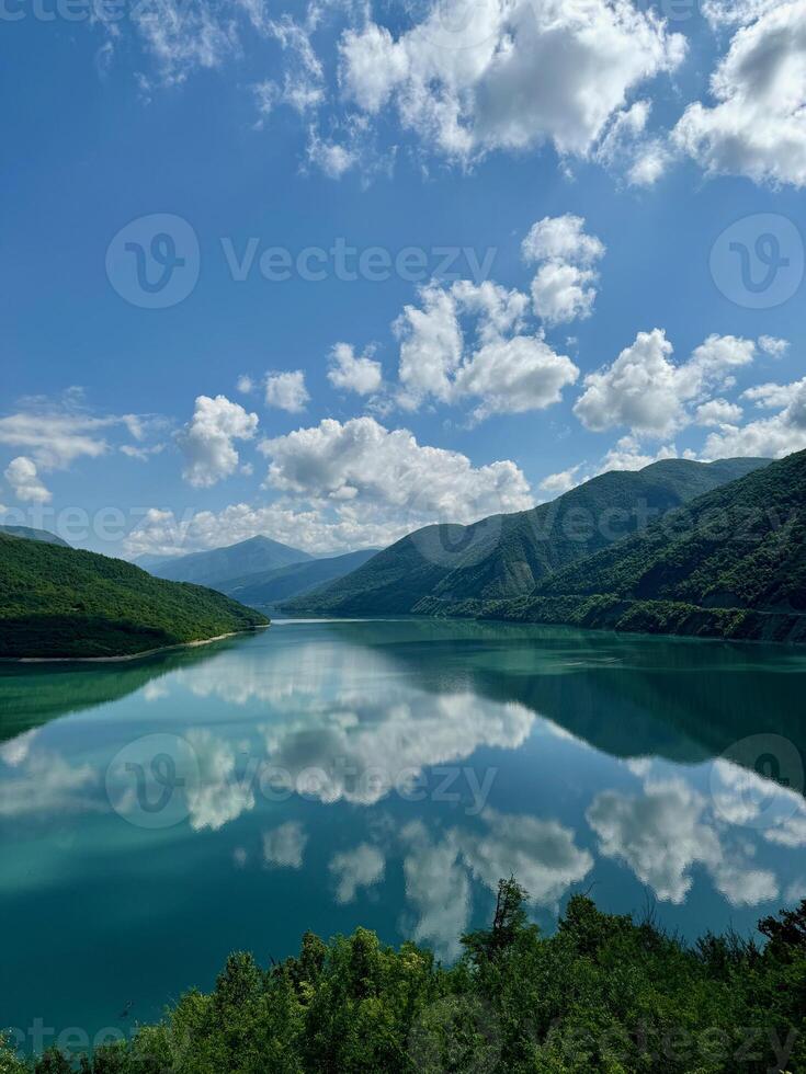 View of a lake between two lushy green hills with reflection of cloudy sky photo