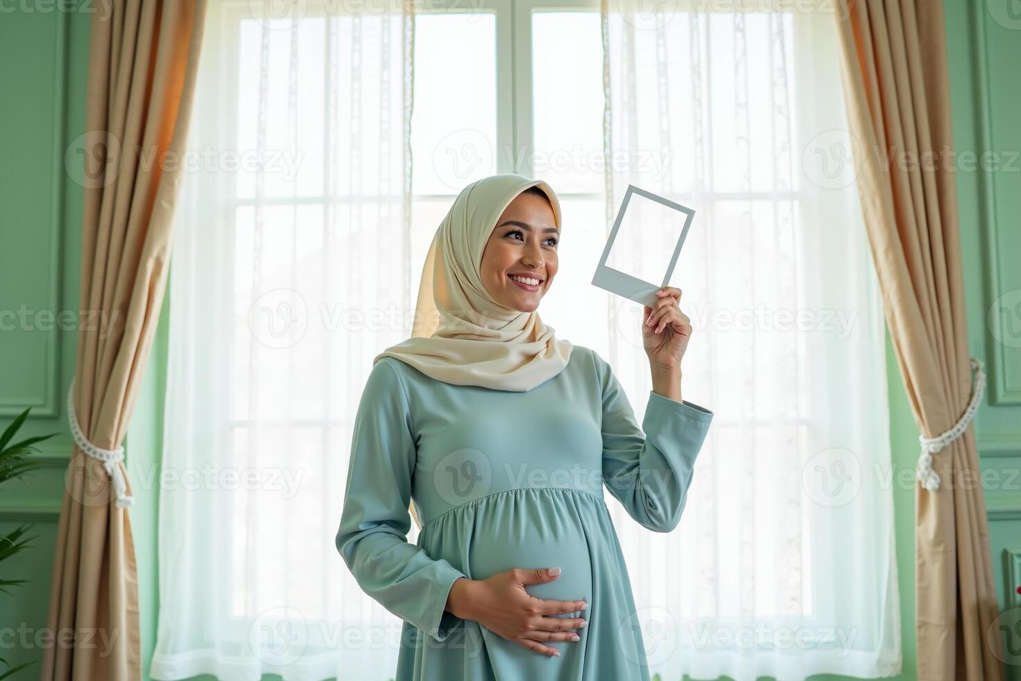 photo of muslim pregnant woman with hijab happy standing holding empty white photograph frame,