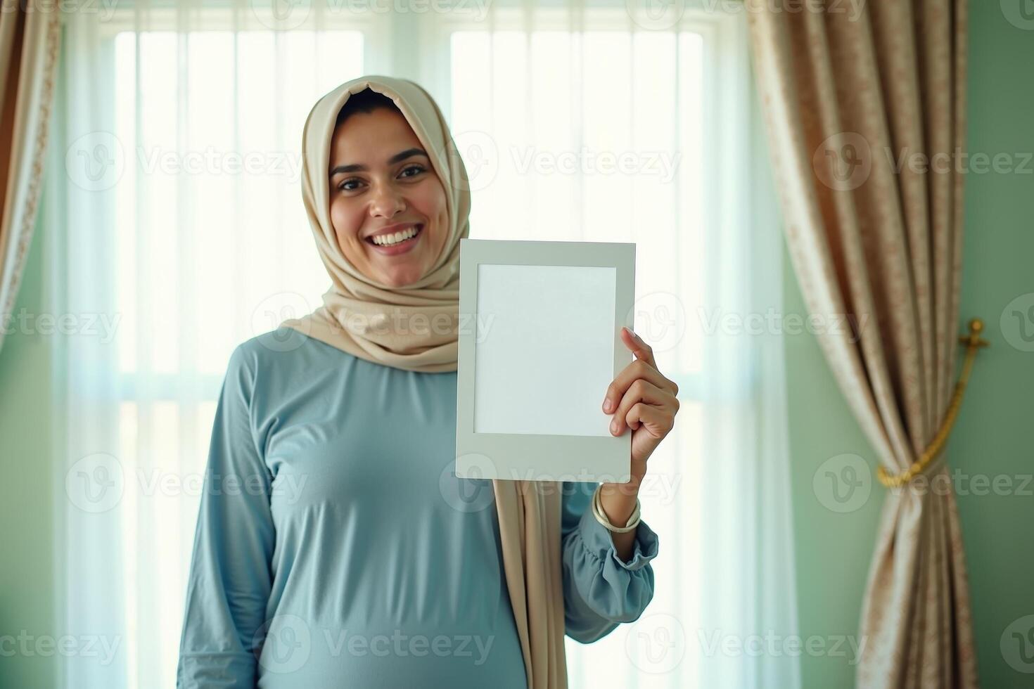 photo of muslim pregnant woman with hijab happy standing holding empty white photograph frame,