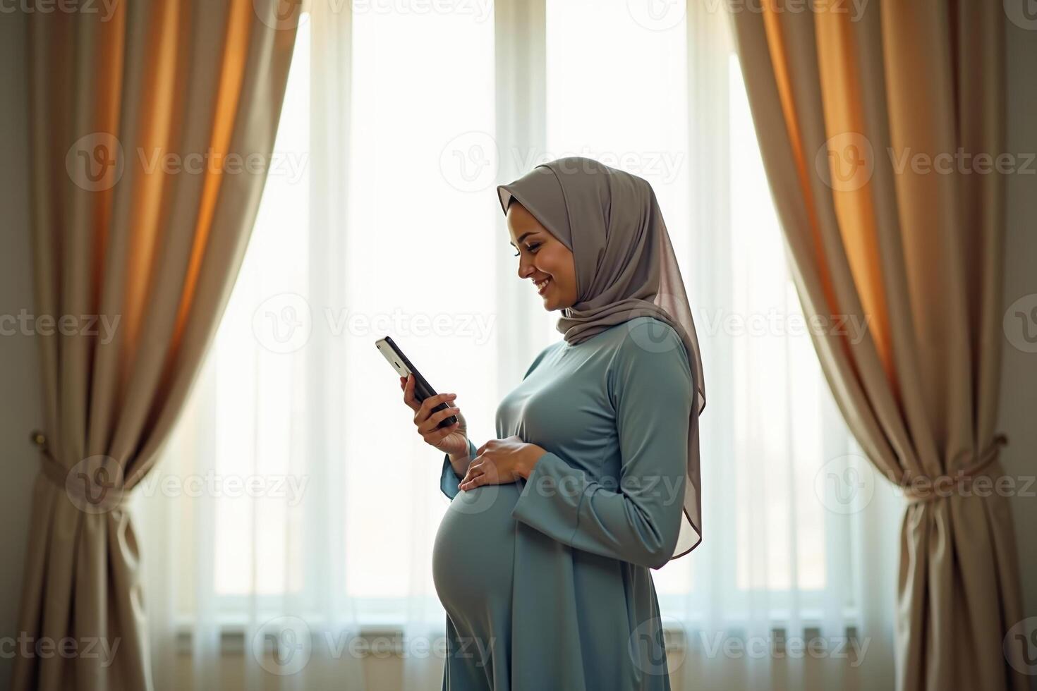 photo of muslim pregnant woman with hijab happy standing holding mobile phone at house,