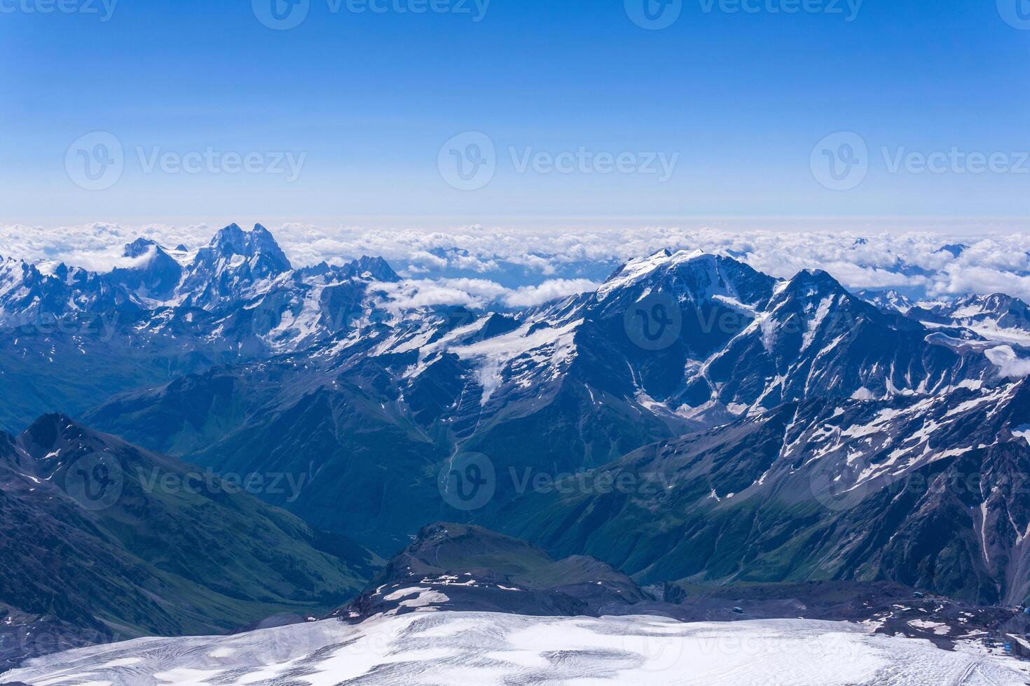 view of the high mountains above the clouds from the snowfield on the slope of Mount Elbrus photo