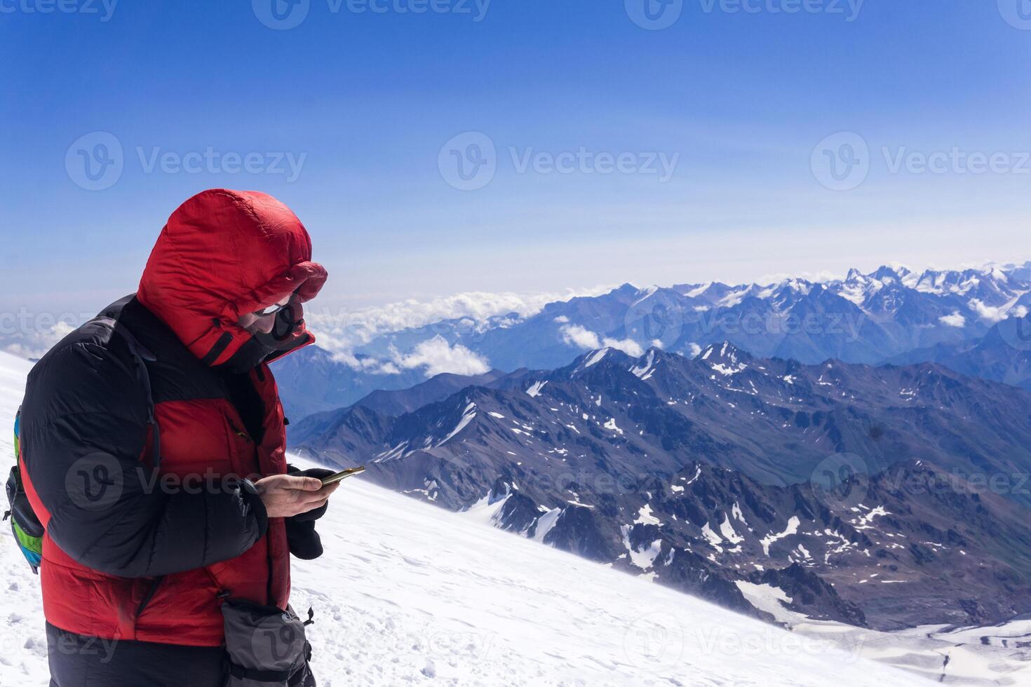 mountain climber looking at smartphone screen while standing on highland snow slope photo