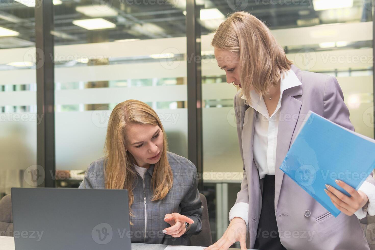 Two young businesswomen working with laptop and documents in workspace. photo
