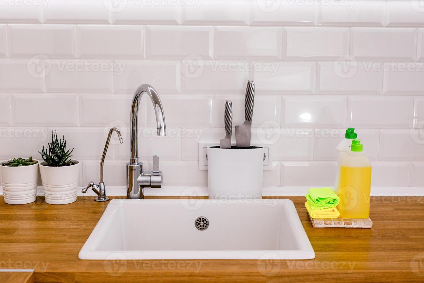 White plates, glass cups and forks in a clean white sink and two bottles of detergent and rags photo