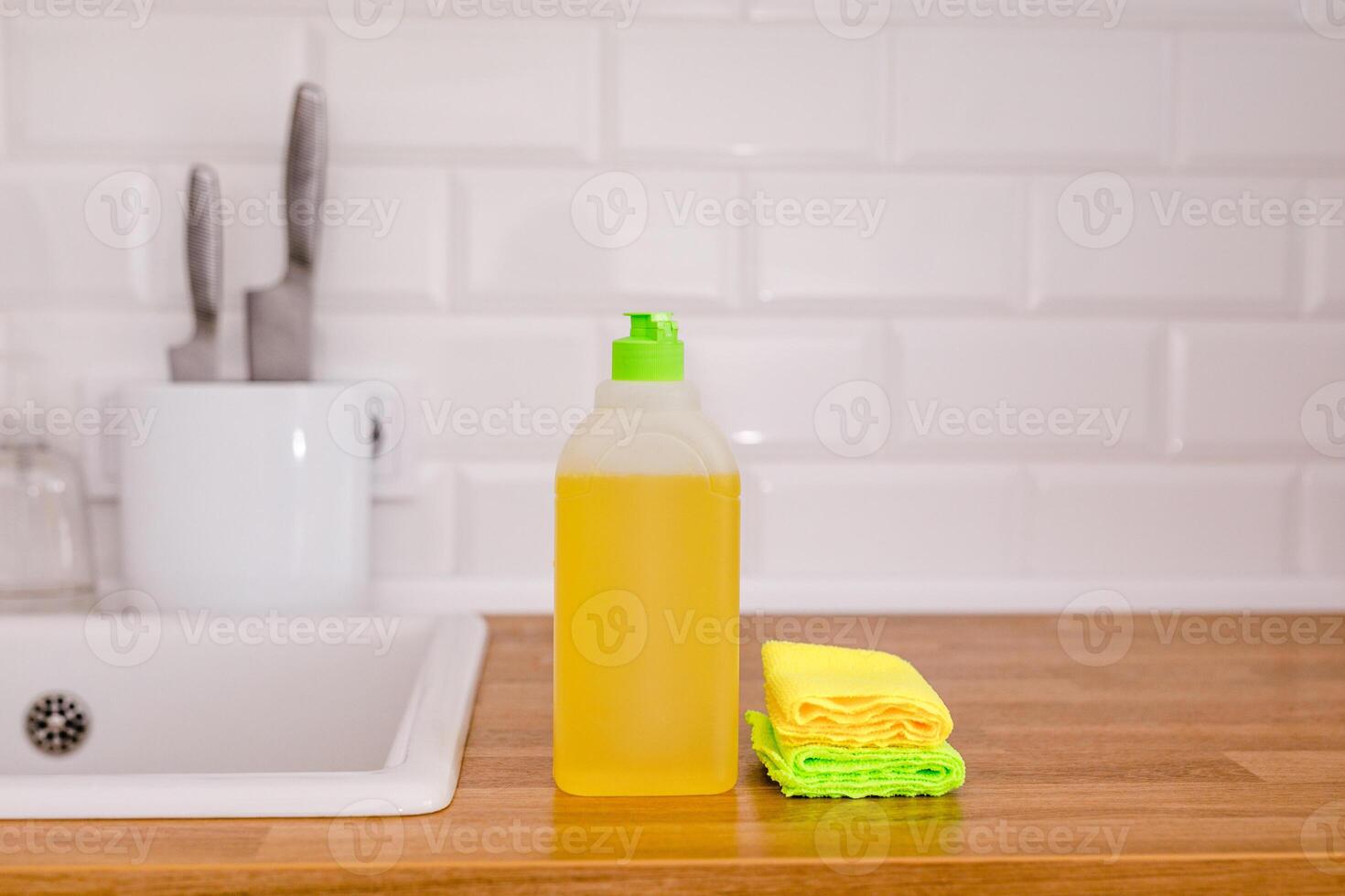 White plates, glass cups and forks in a clean white sink and two bottles of detergent and rags photo