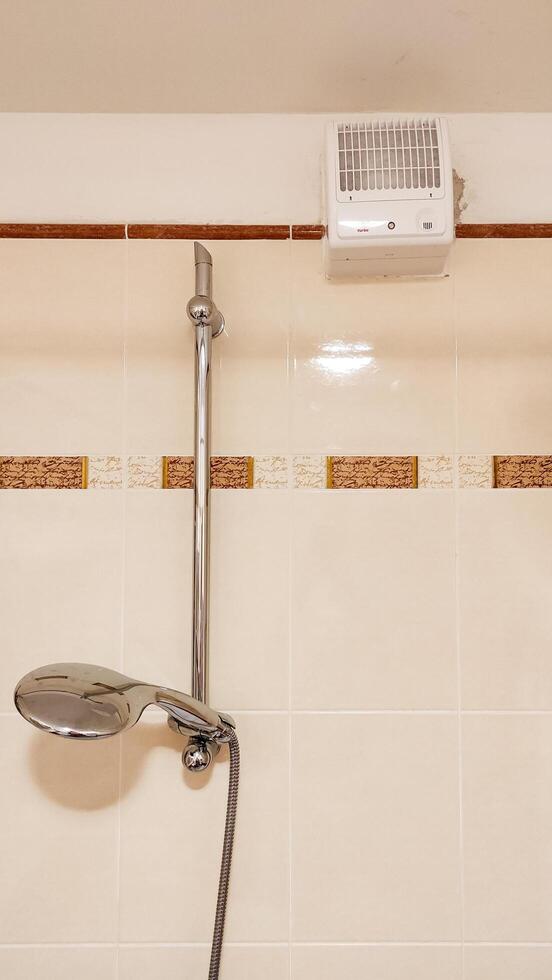 Prague, Czech republic - October 6, 2023. A sleek chrome showerhead with a bathroom exhaust Vents turbo fan above it photo