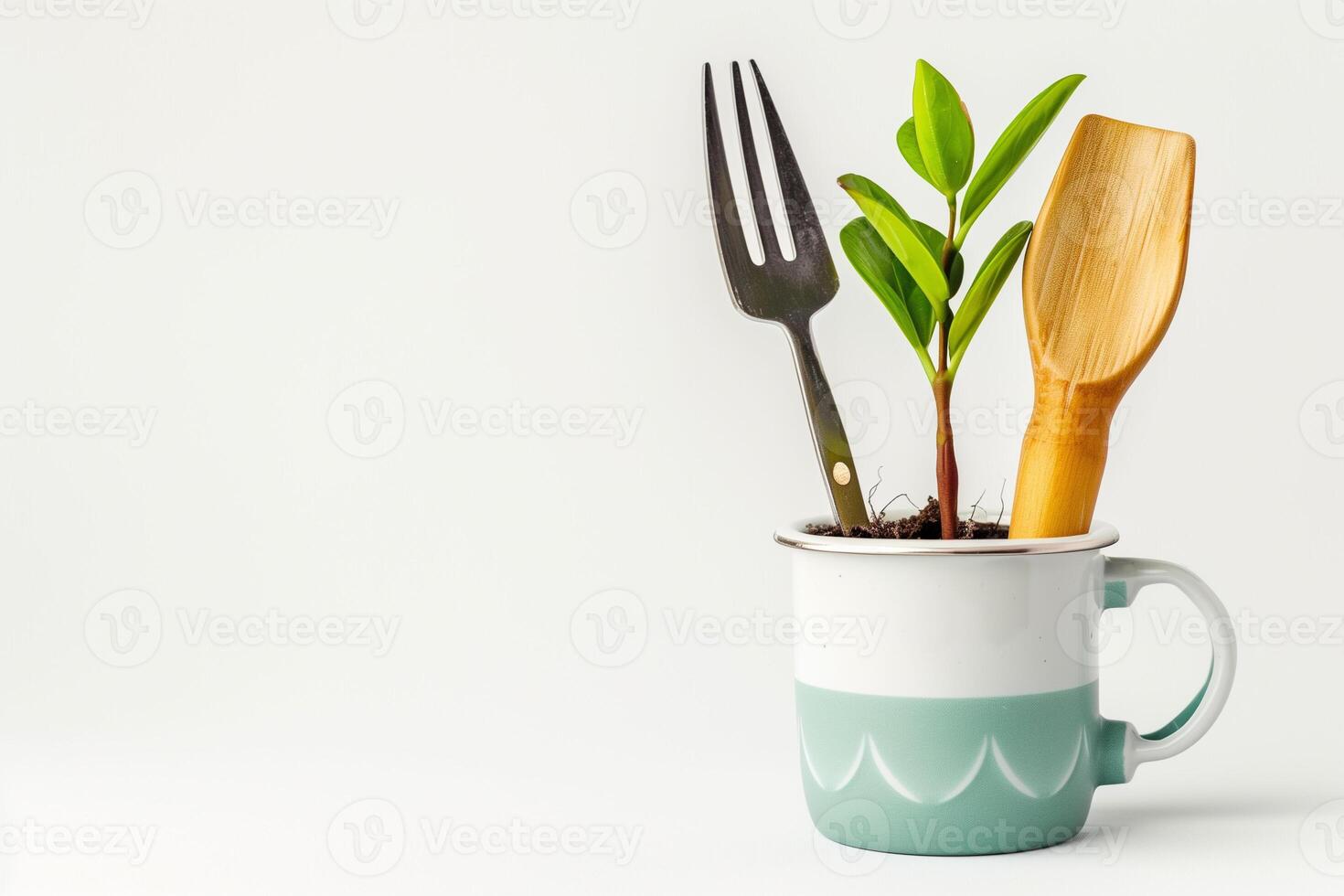 A green plant growing in a white and teal mug with a fork and wooden spoon photo