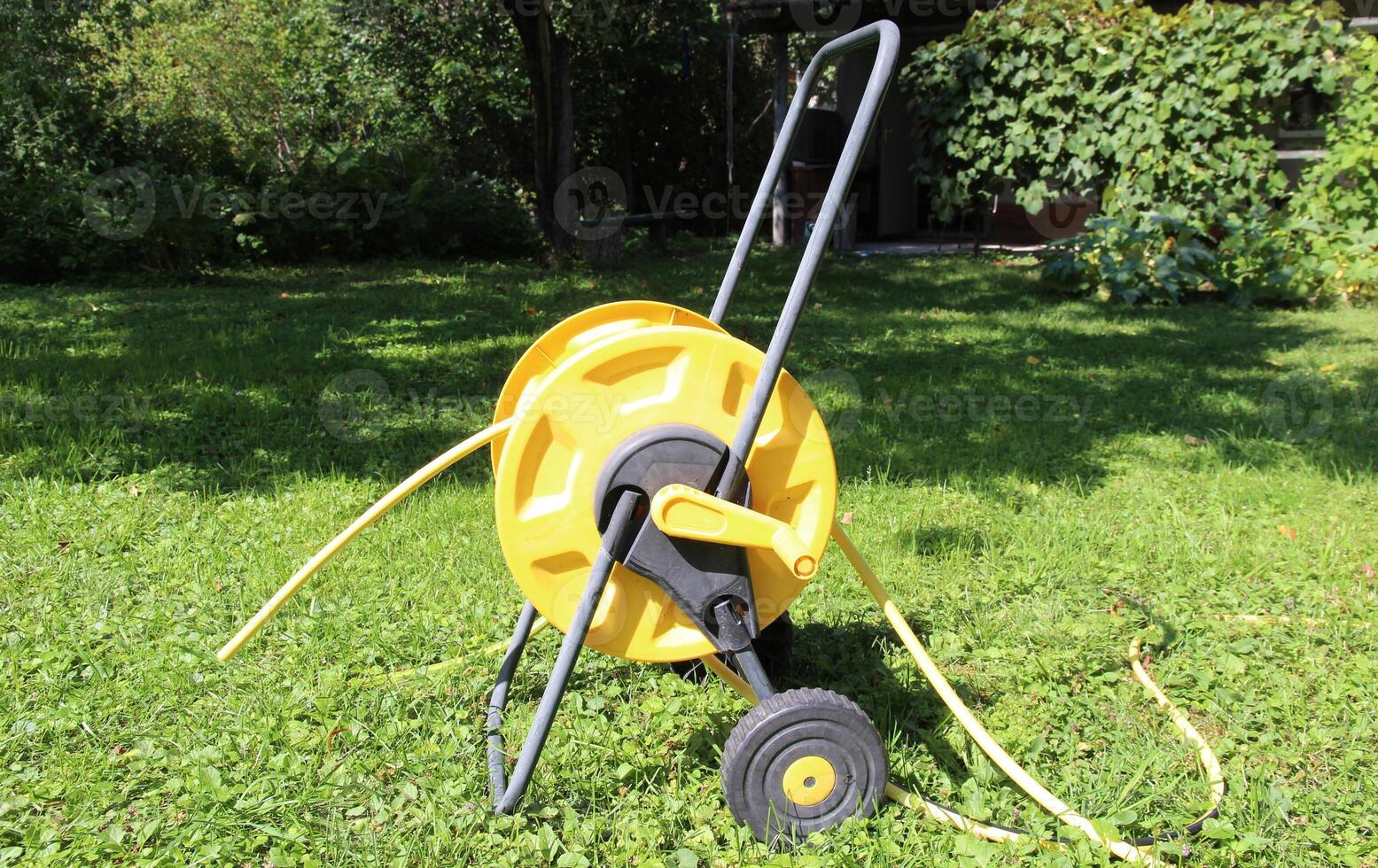 bright yellow garden hose reel with a handle and wheels stands on lush green grass, on the lawn. Ideal for illustrating garden maintenance, landscaping services, or DIY gardening projects. photo