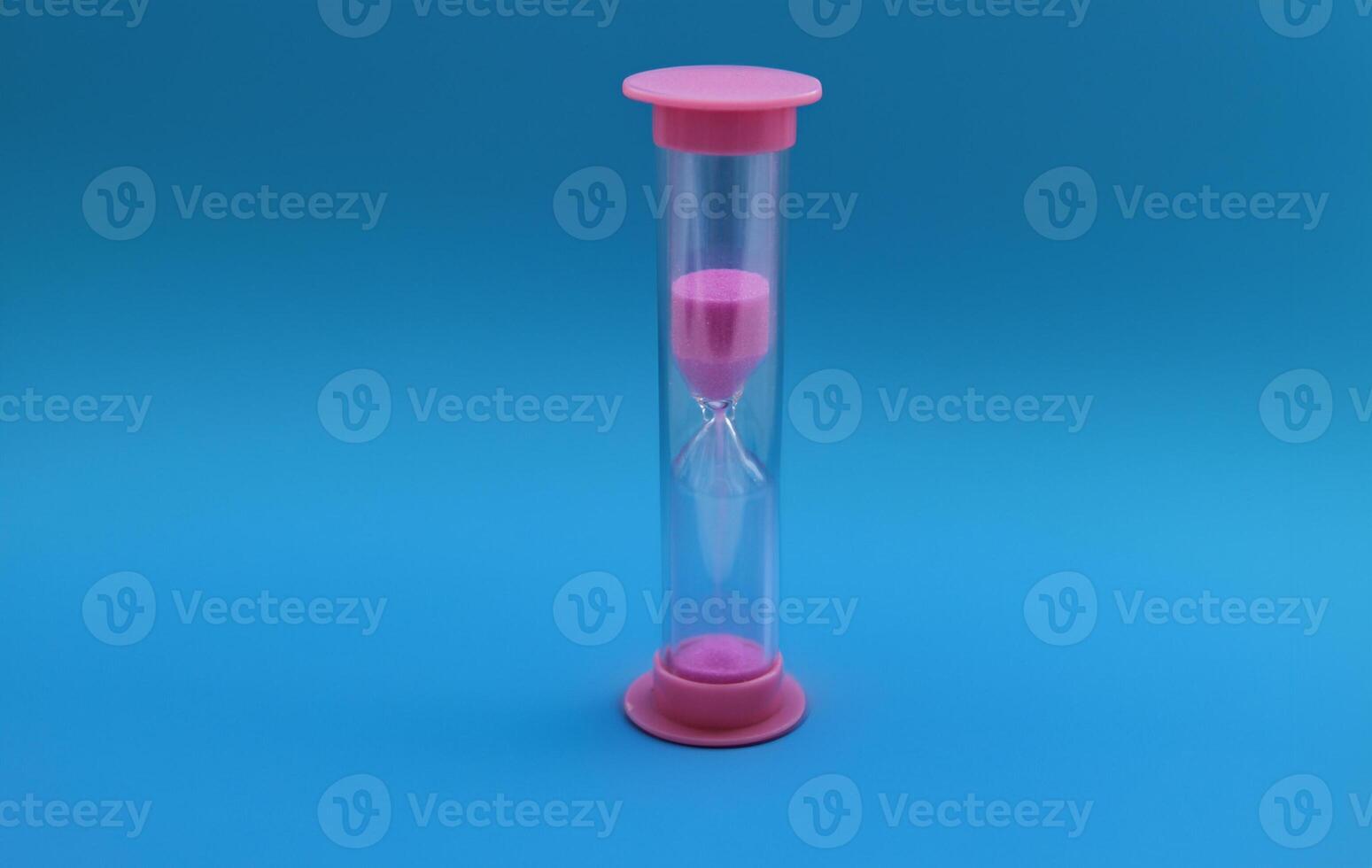 Pink hourglass with flowing grains of sand isolated on a blue background. Time concept. photo