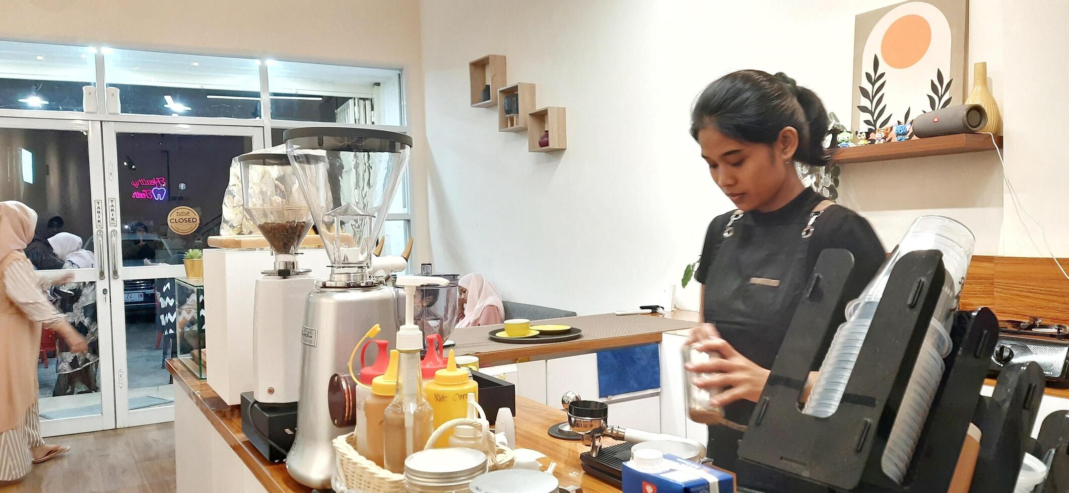 Close up Barista making coffee for customer in cafe. Woman working in coffee shop wearing an apron. Makassar, South Sulawesi, Indonesia - August 11 2024 photo