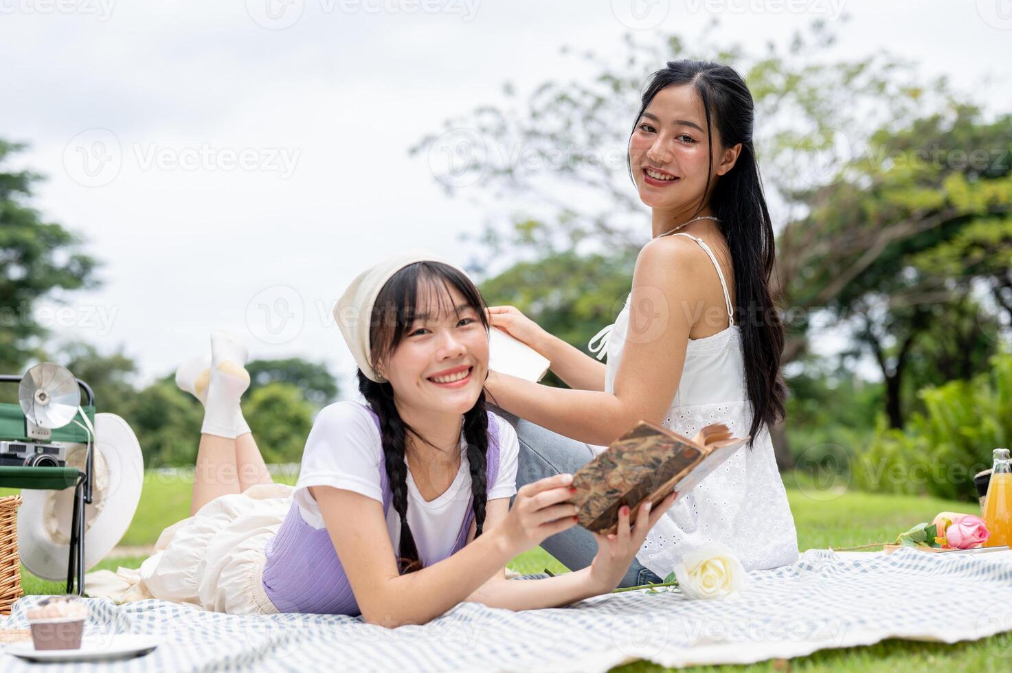 Lovely Asian woman lies on a picnic blanket, reading a book while enjoying a picnic with her friend. photo