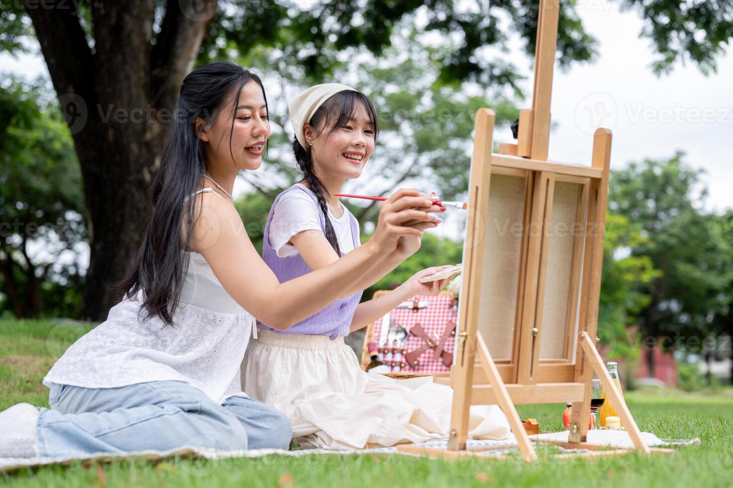 Two positive and lovely young Asian women are enjoying painting on a canvas easel together in a park photo