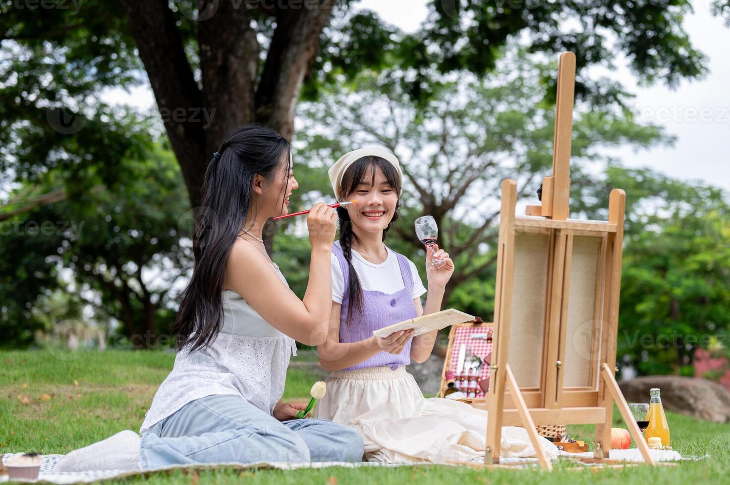 Two positive and cute Asian best friends are enjoying painting on a canvas easel together in a park. photo