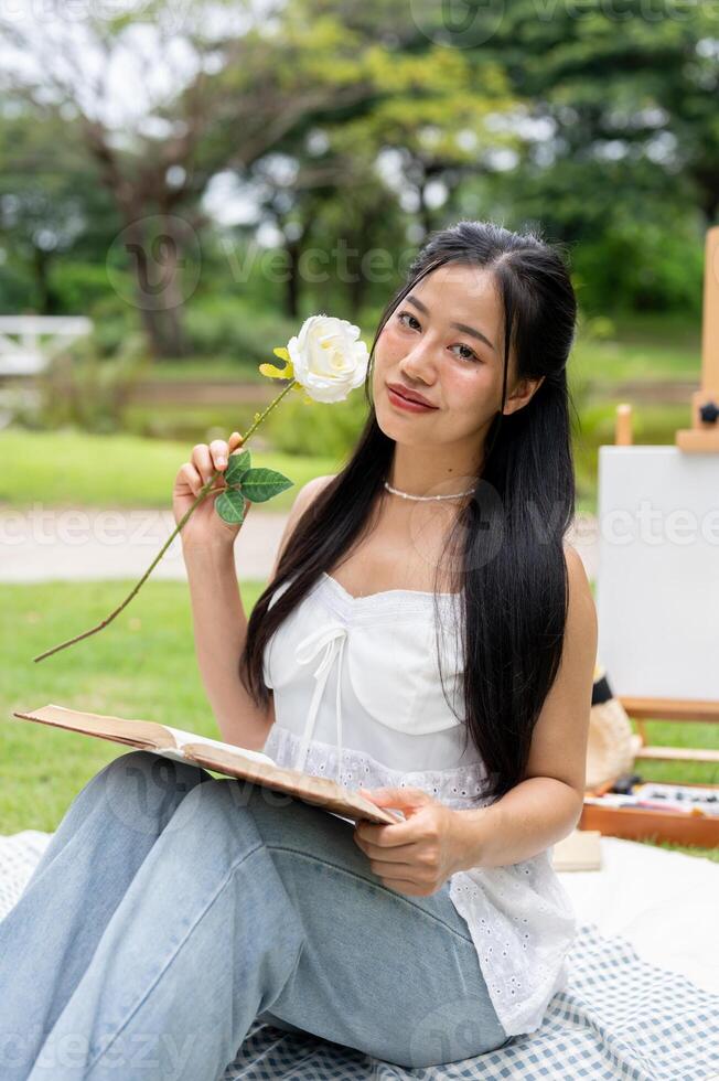 A beautiful Asian woman sitting on a picnic blanket in a park, posing and smiling at the camera. photo