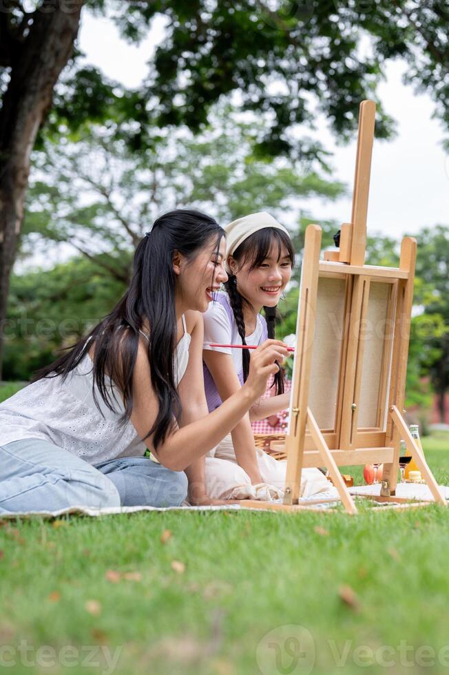 Two positive and cute Asian best friends are enjoying painting on a canvas easel together in a park. photo