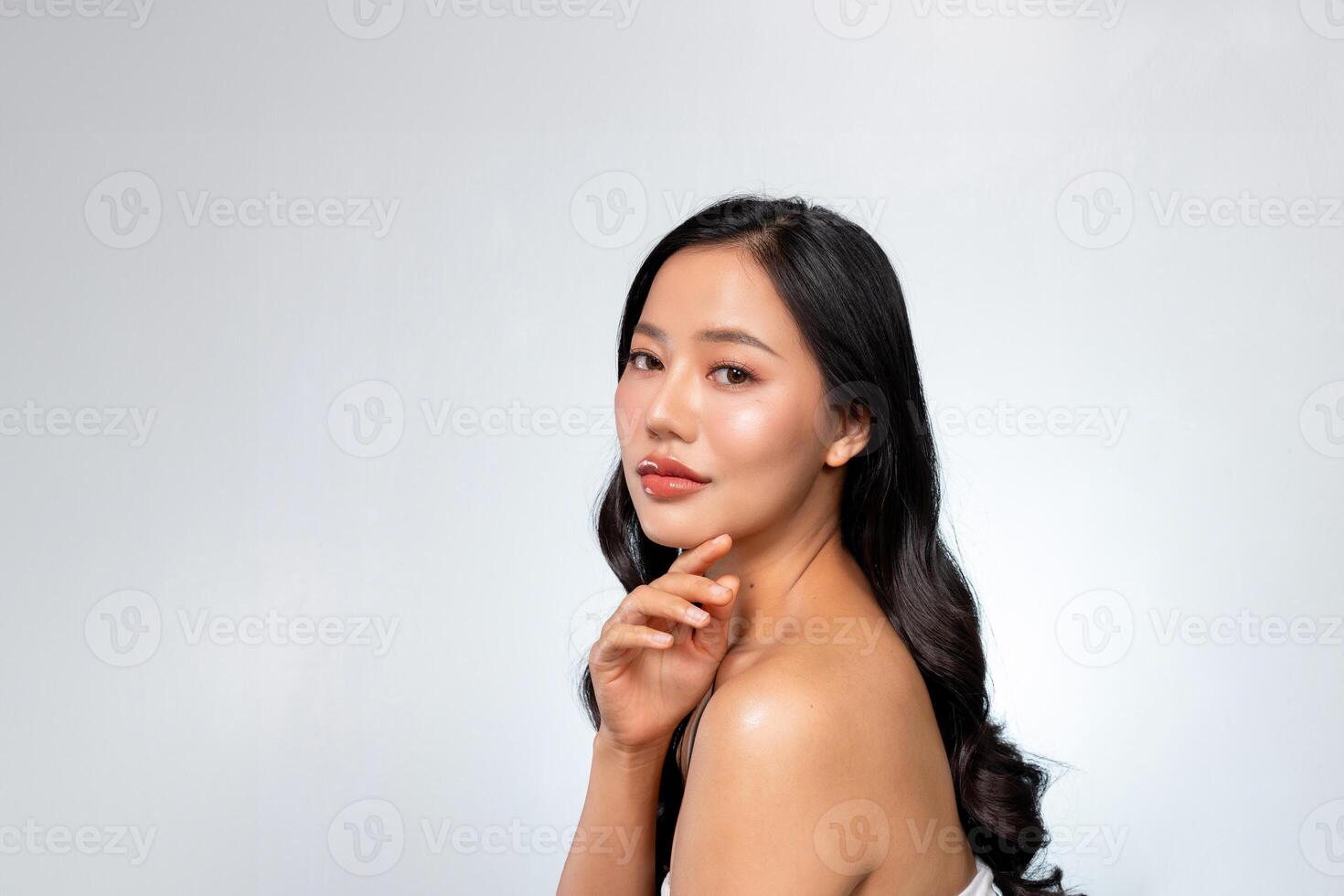Elegant Asian woman poses against a grey background, looking at the camera while touching her chin. photo