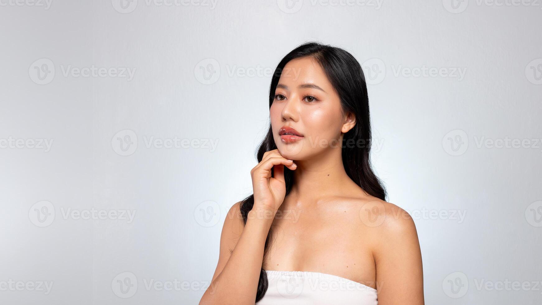 Gorgeous Asian woman with a beautiful face poses against a grey background, gently touching her chin photo