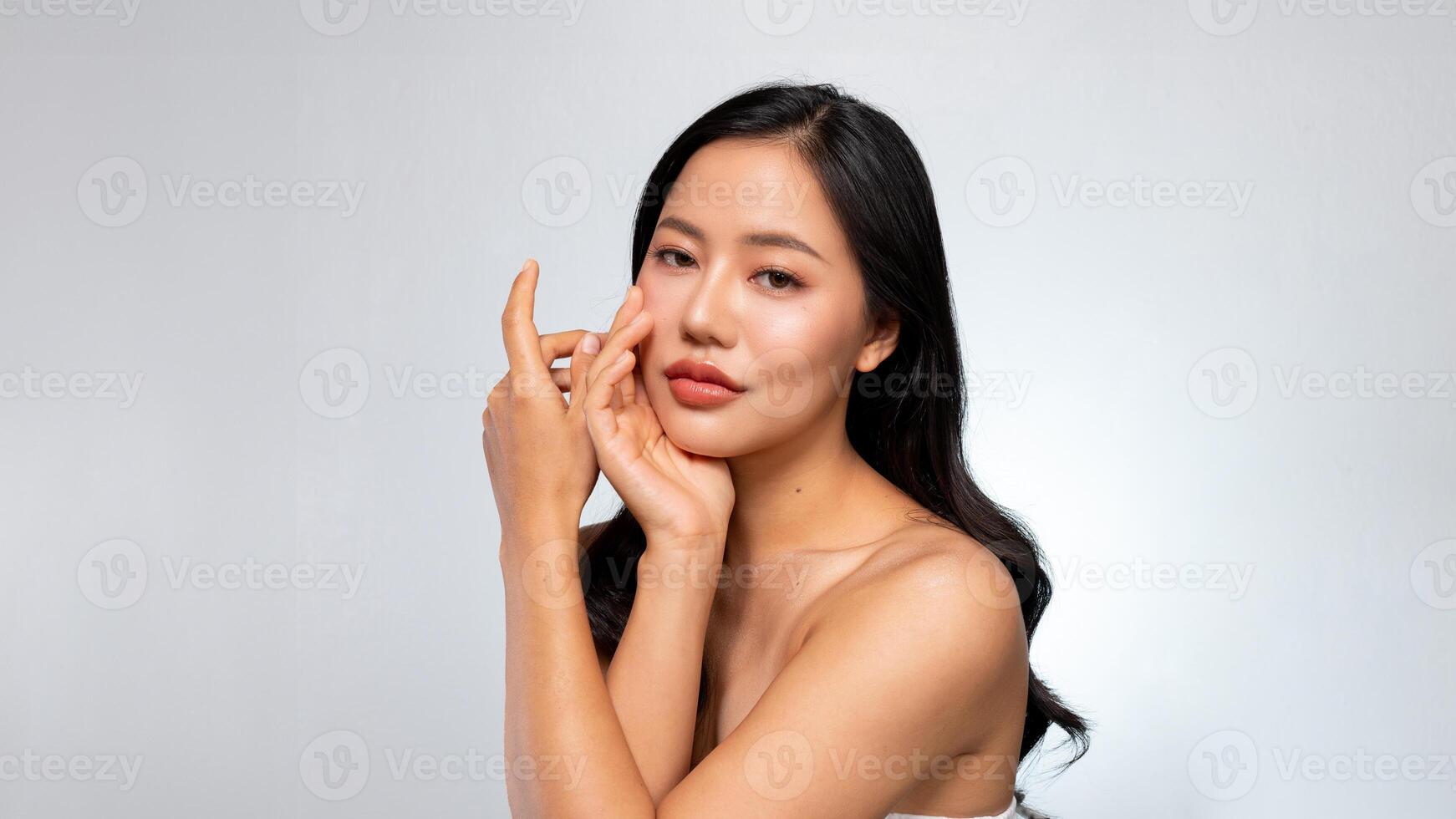 An elegant Asian woman poses with her hand on her chin against a grey background. photo