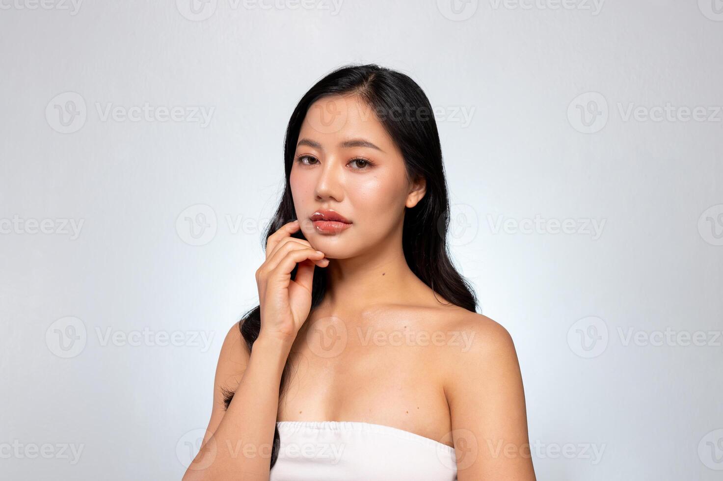 Gorgeous Asian woman with a beautiful face poses against a grey background, gently touching her chin photo