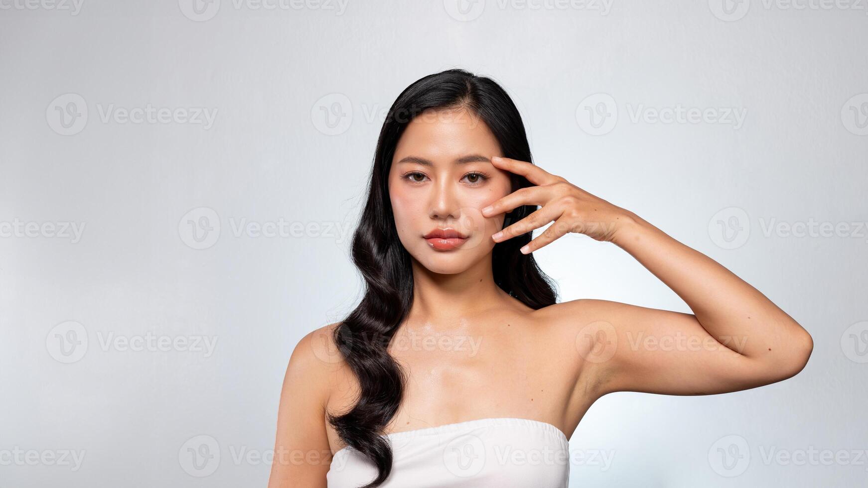 A gorgeous Asian woman poses against a grey background, touching her flawless facial skin. photo