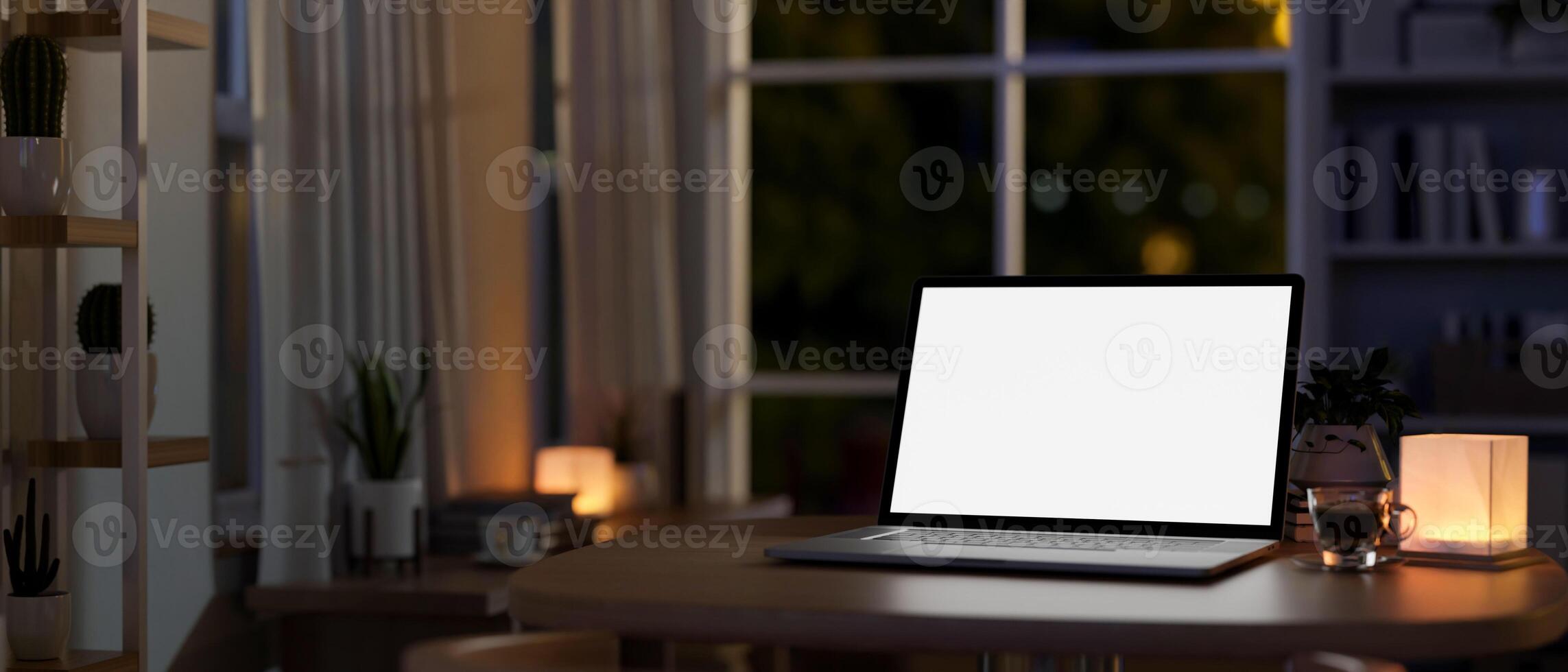 A laptop computer on a table in a room at home at night, illuminated by a table lamp. photo