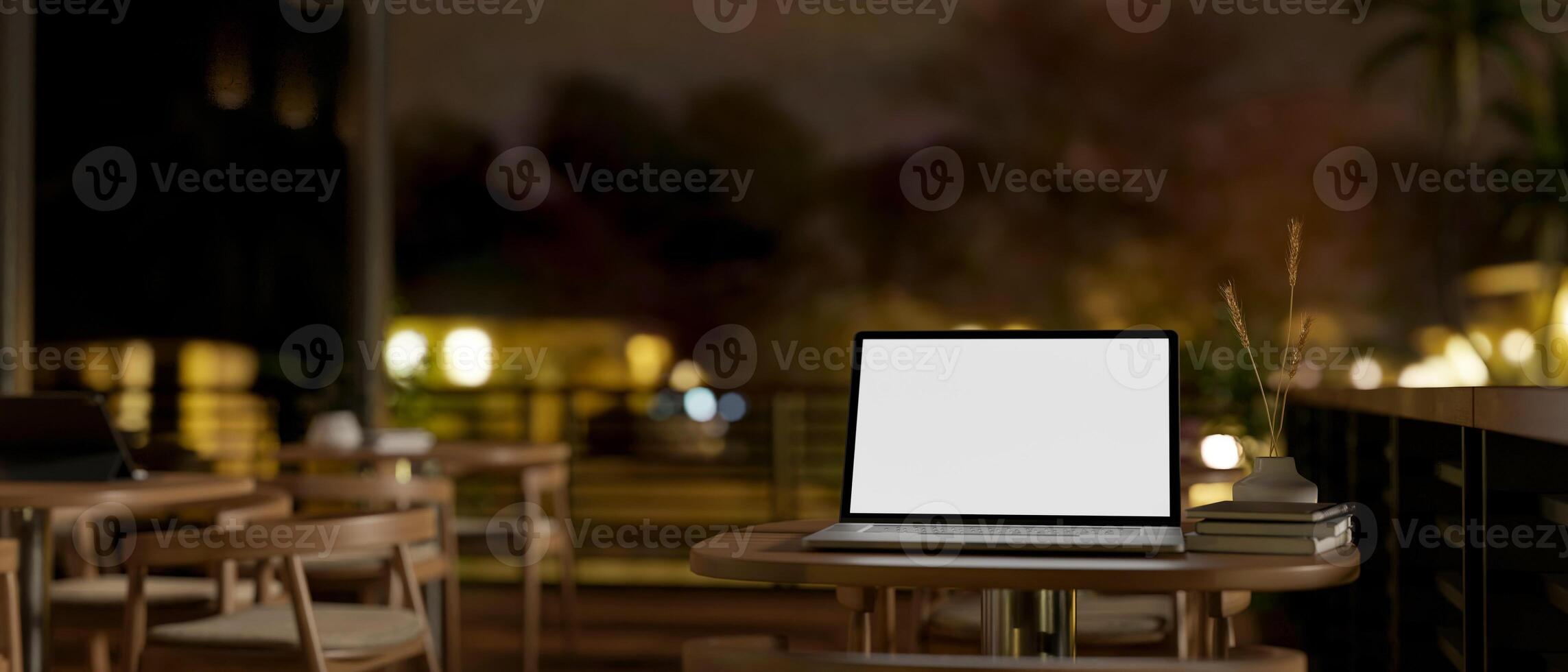 A laptop computer mockup on a table on an outdoor terrace of a coffee shop at night. photo