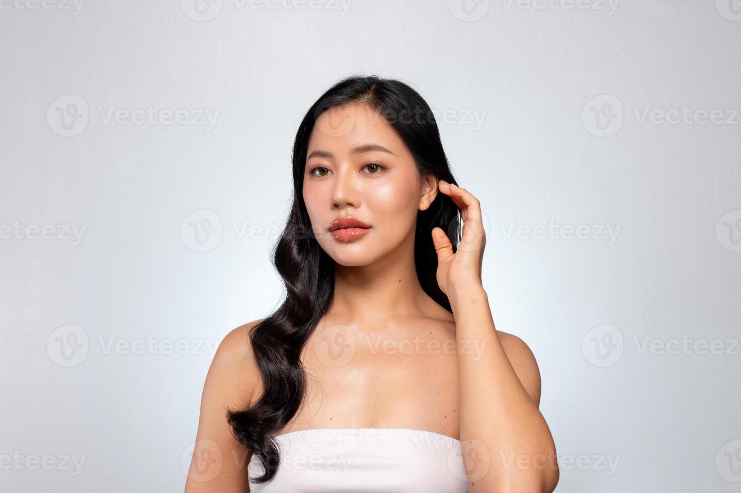 Beautiful Asian woman with healthy black curly hair and tanned skin poses against a grey background. photo