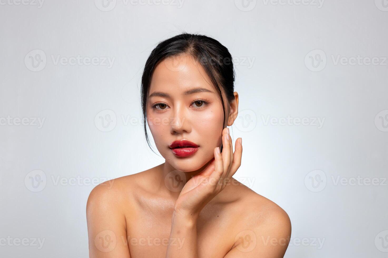 A beautiful Asian woman with red lips, and tanned skin poses against an isolated grey background. photo